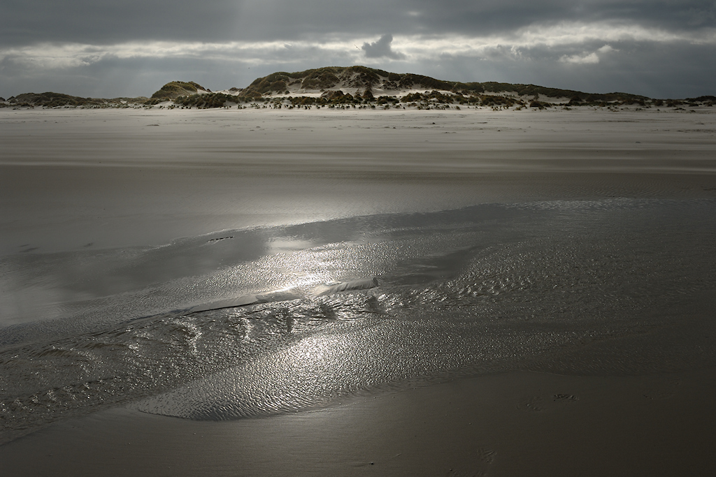 Na een golf trekt water zich terug van het strand